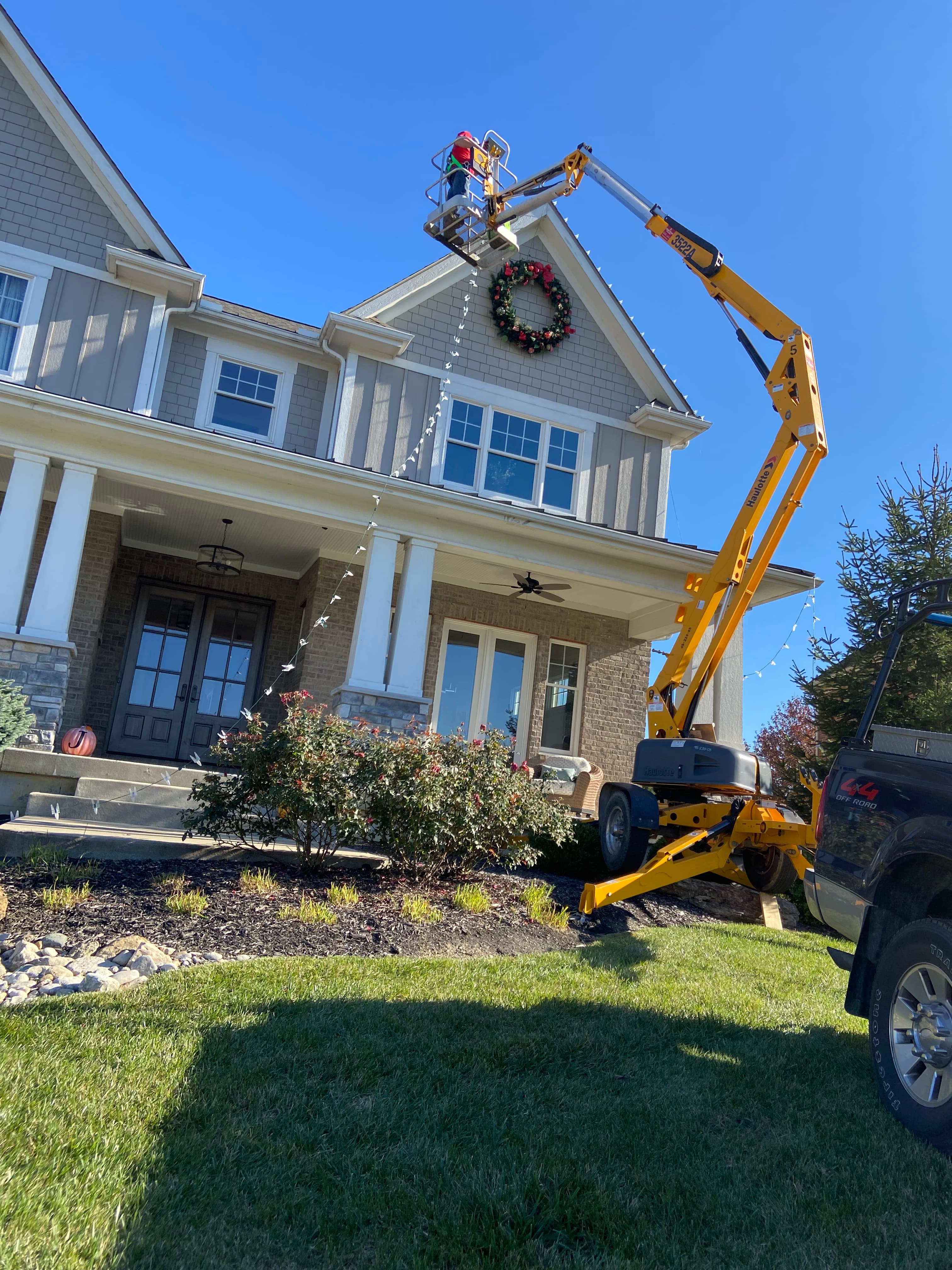 Crew member using a lift to install a large Christmas wreath on a home