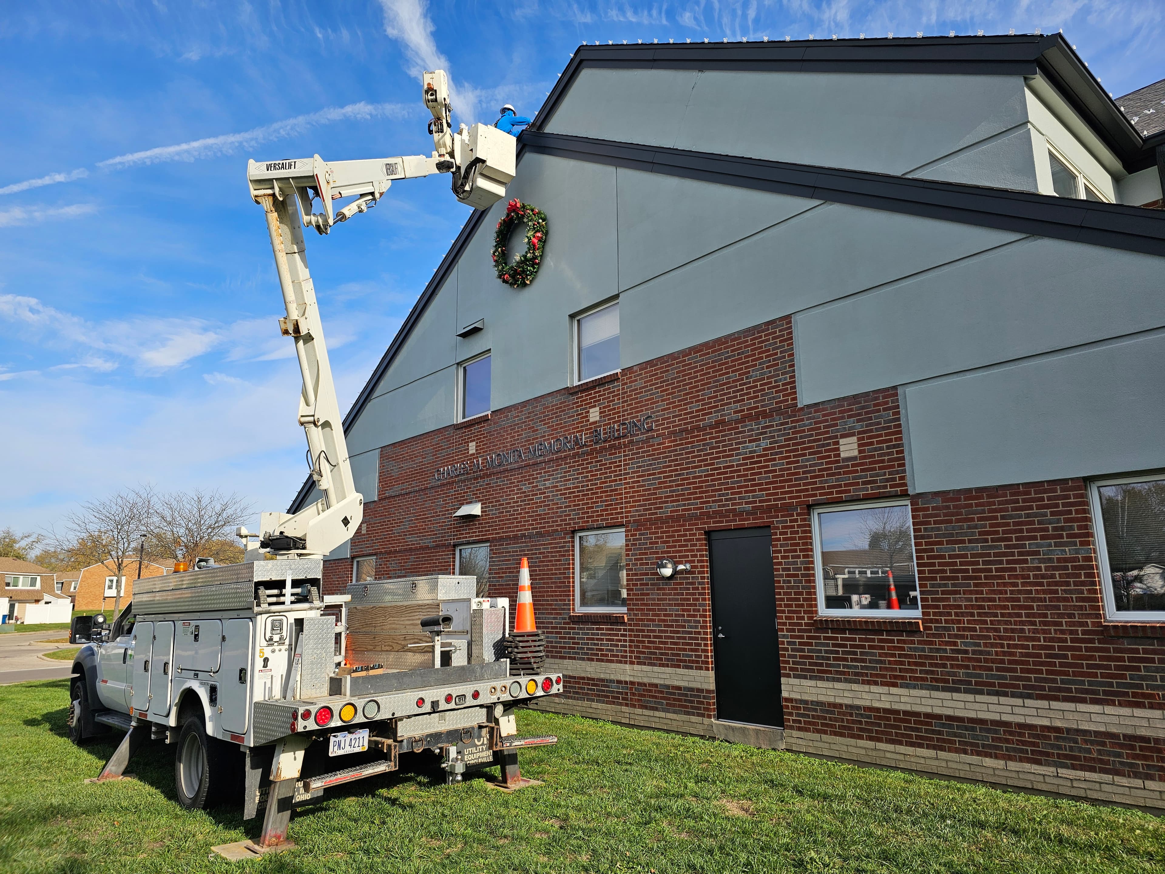 Bucket truck crew installing a wreath and roofline lights on a municipal building