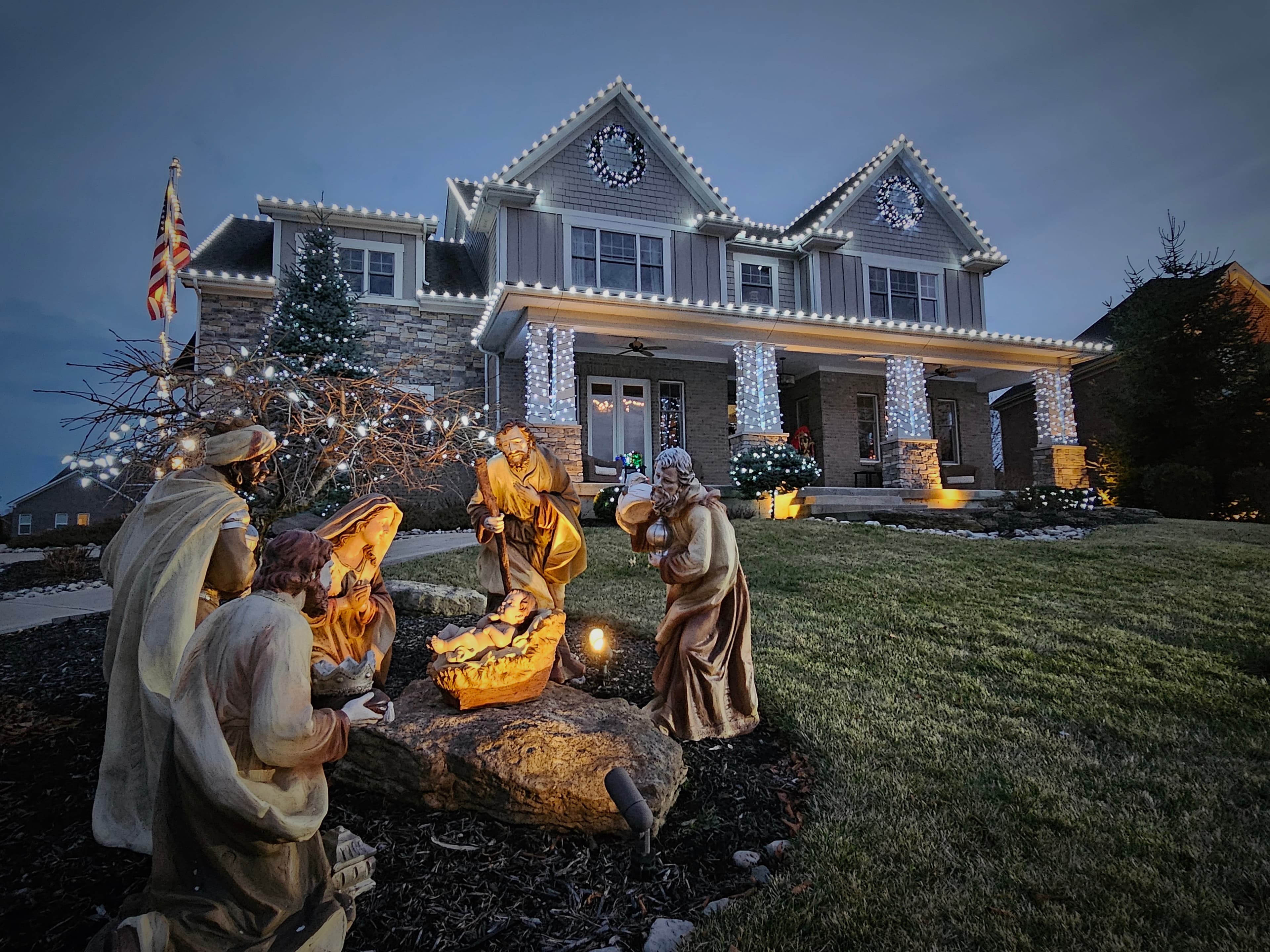 Warm-white residential roofline, wreaths and columns with a finished nativity display