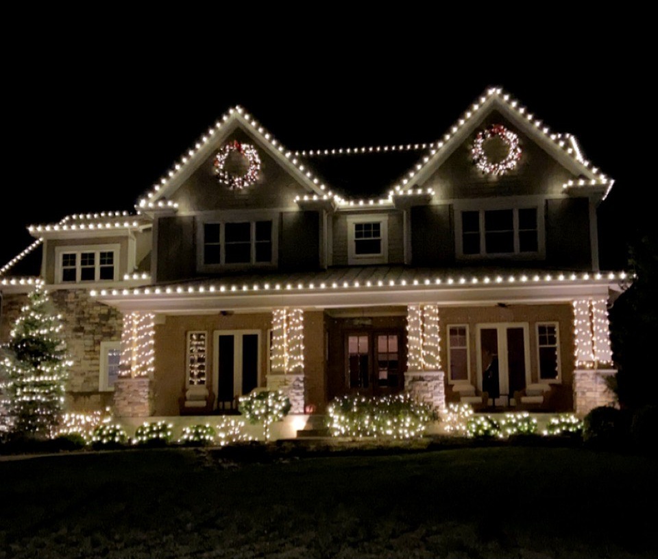 Large residence finished with warm-white roofline, wreath, column, and landscape lighting