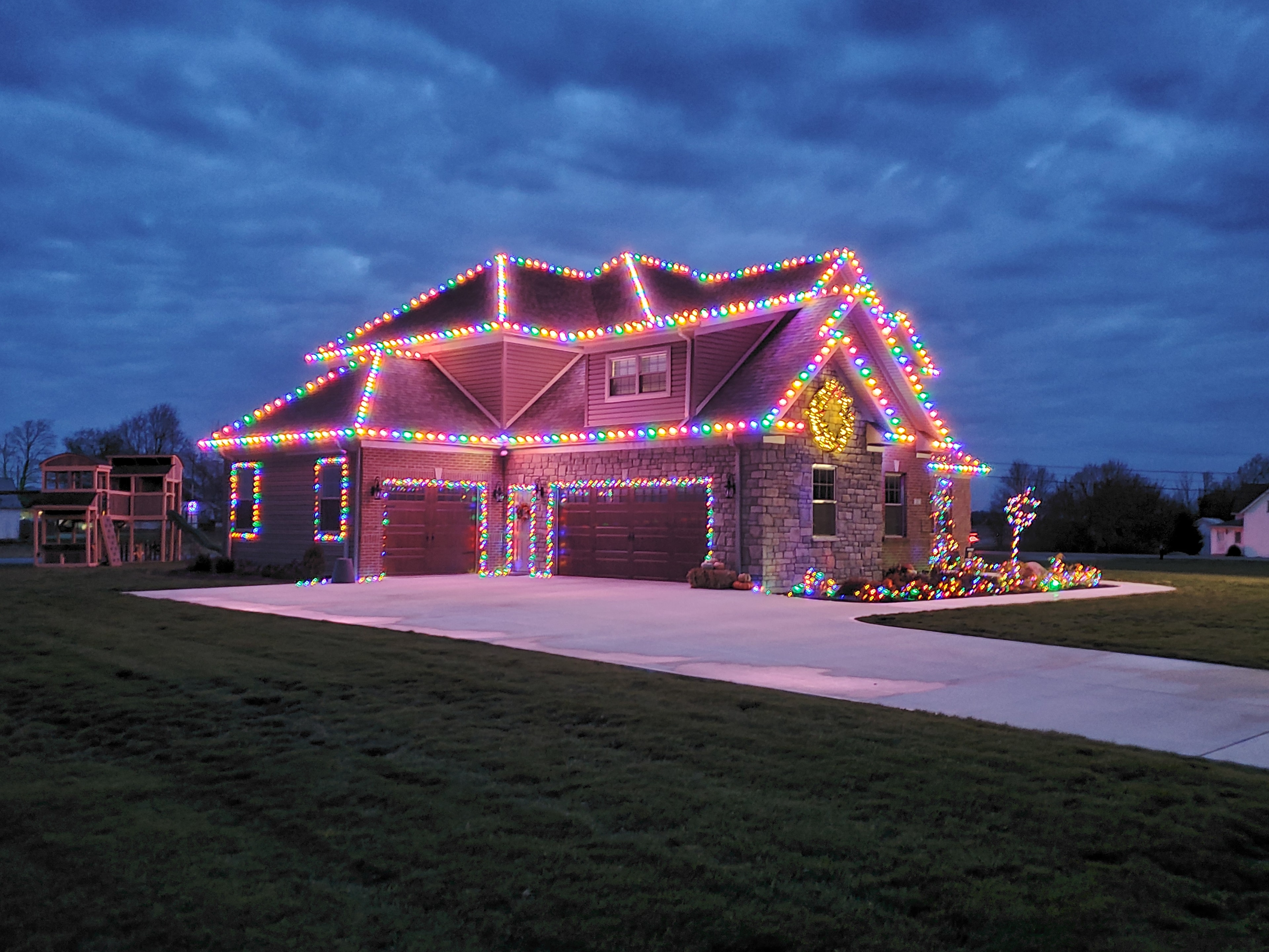 Large home outlined in bright multicolored Christmas lights at dusk