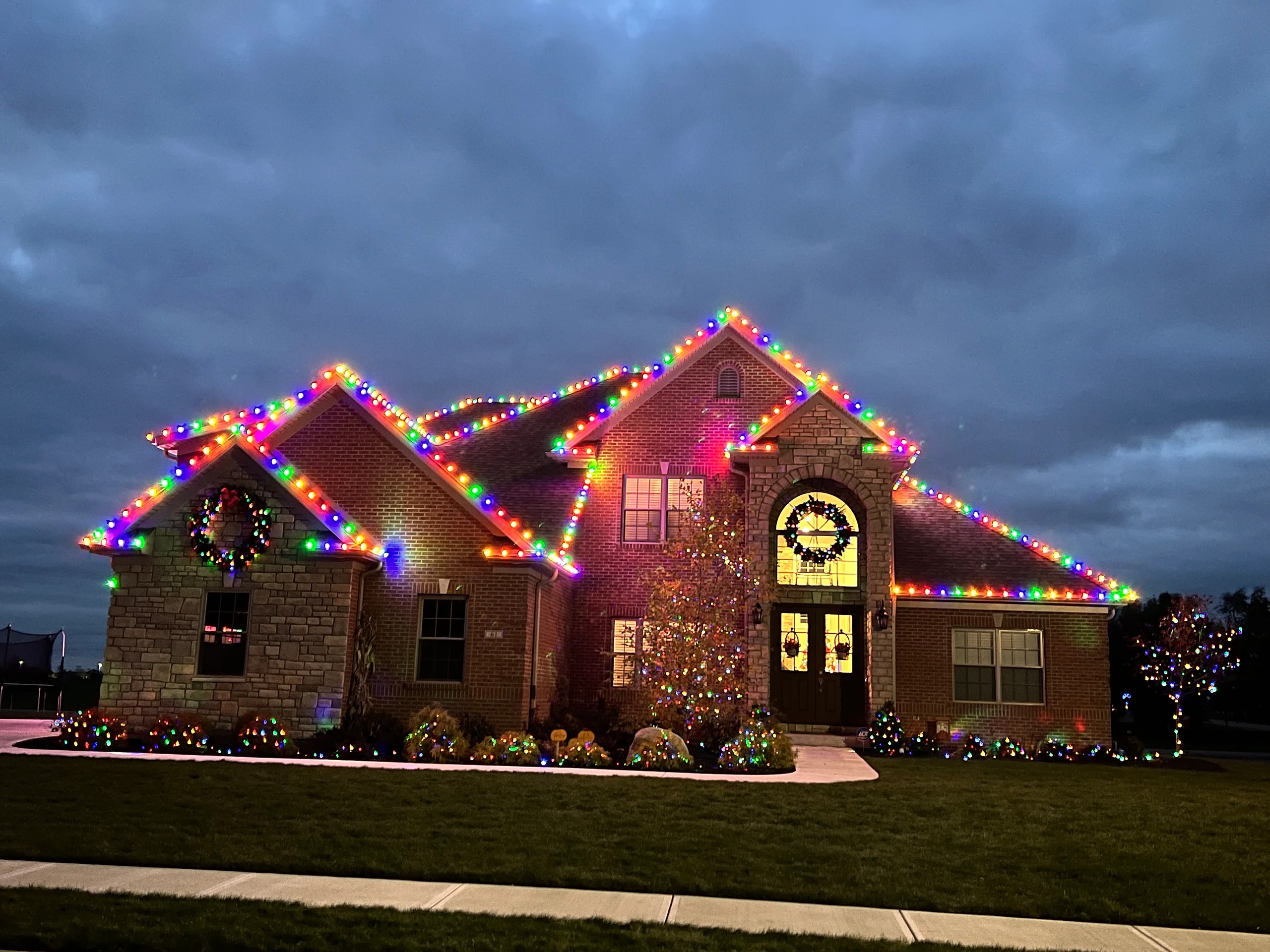 Large residence with multicolored rooflines, wreaths, and landscape lighting at twilight