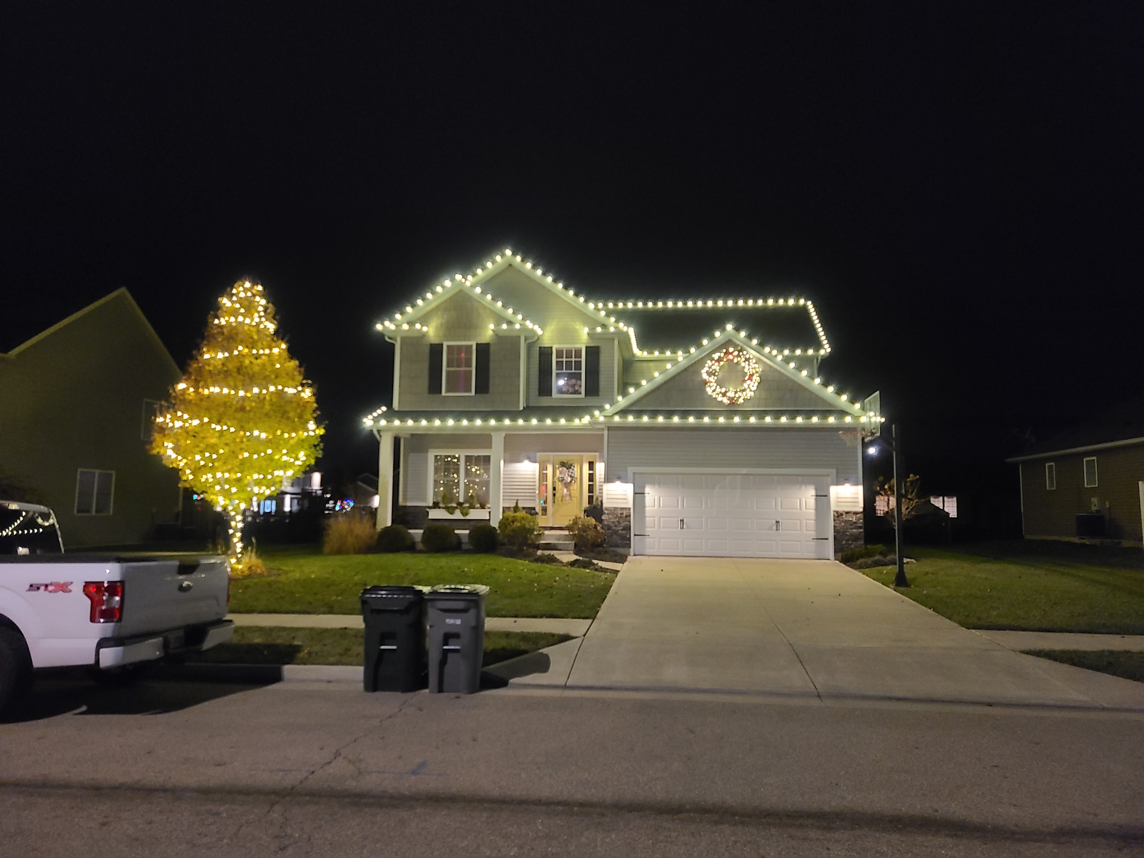 Two-story home and large tree illuminated with warm-white Christmas lights